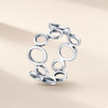 Bague Ricochets argent 925, une suite de cercles évidés, petits et grands, reliés les uns aux autres tout autour du doigt, sans pierre, sur fond crème