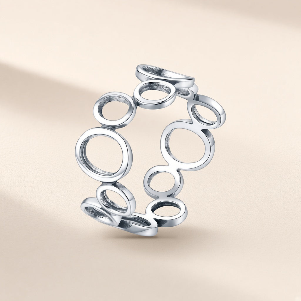 Bague Ricochets argent 925, une suite de cercles évidés, petits et grands, reliés les uns aux autres tout autour du doigt, sans pierre, sur fond crème