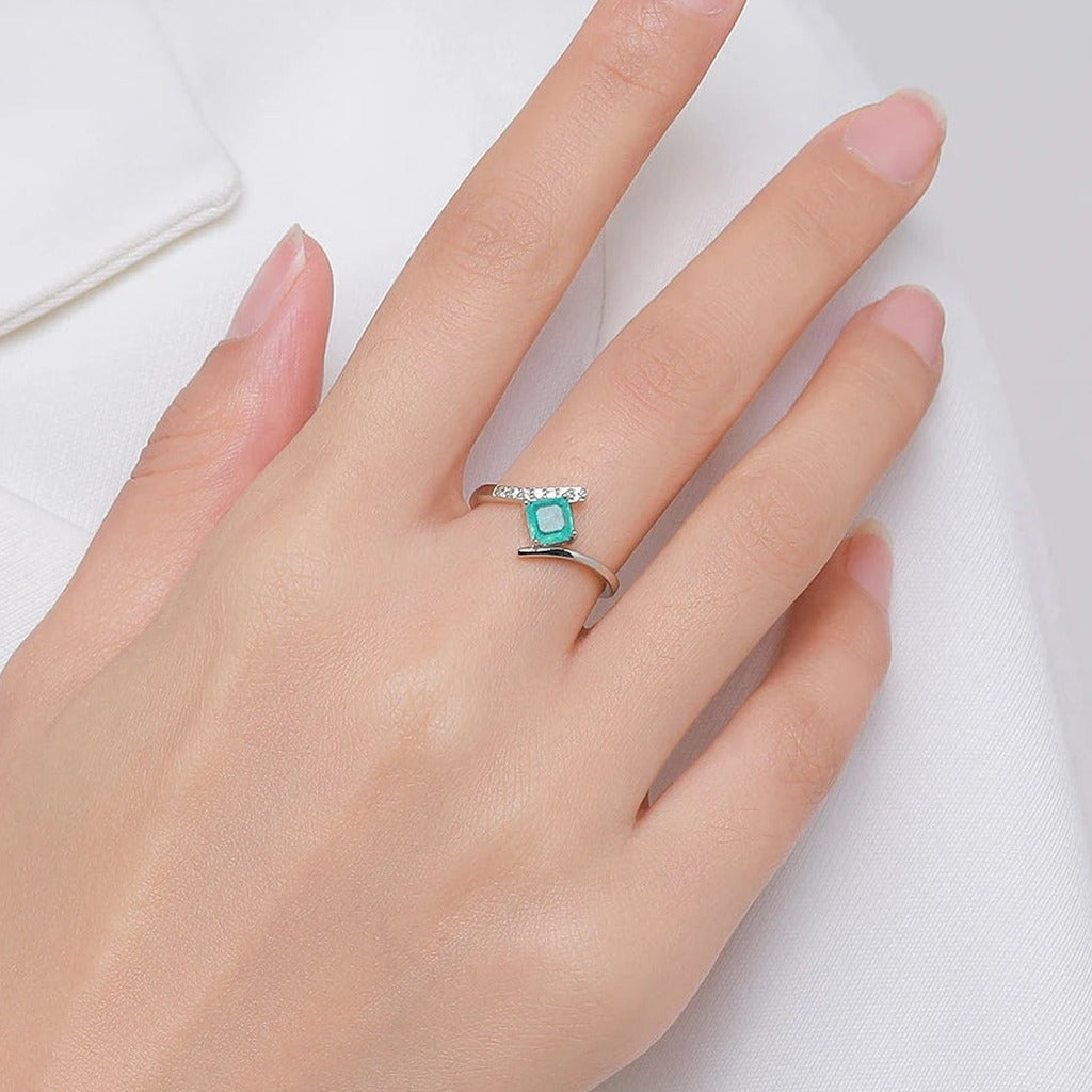 Bague Calanque portée au doigt : la pierre carrée bleu-vert vue de dessus, main posée sur un tissu blanc