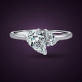 Bague Giboulée argent 925, deux zirconiums cubiques incolores taillés en goutte, un grand et un petit, posés tête-bêche sur un anneau fin, sur fond aubergine