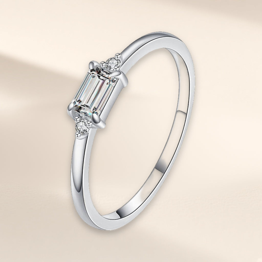 Bague Sentier argent 925, modèle pierre incolore : une pierre d'imitation rectangulaire posée dans le sens de l'anneau, un petit zirconium cubique de chaque côté, sur fond crème