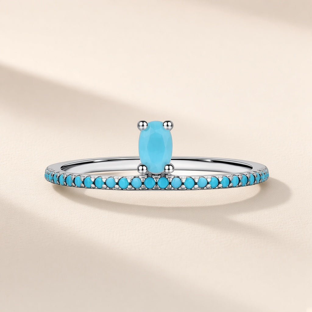 Bague Ruban d'Azur argent 925, pierre d'imitation ovale bleu turquoise sur un anneau fin pavé de petites pierres bleues, sur fond crème