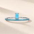 Bague Ruban d'Azur argent 925, pierre d'imitation ovale bleu turquoise sur un anneau fin pavé de petites pierres bleues, sur fond crème