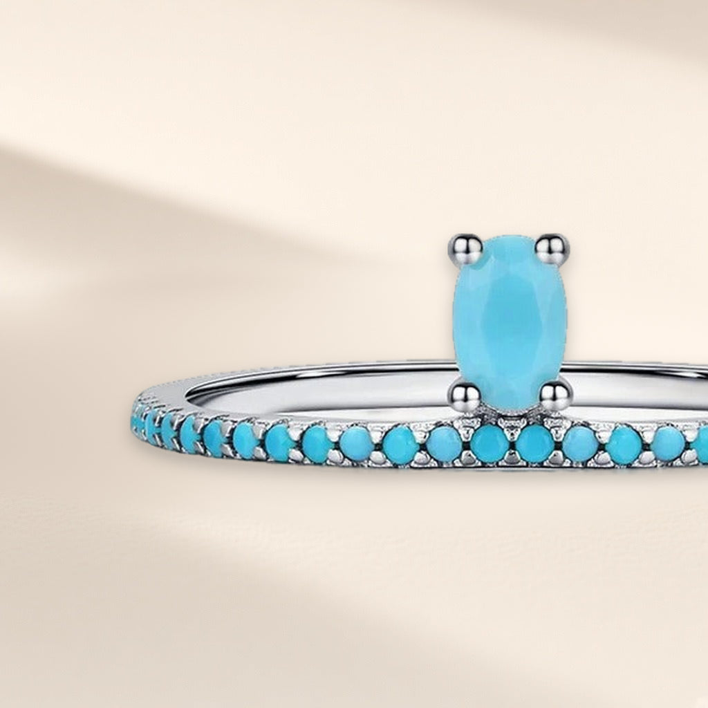 Bague Ruban d'Azur vue de face : pierre ovale turquoise à quatre griffes sur un anneau de petites pierres turquoise