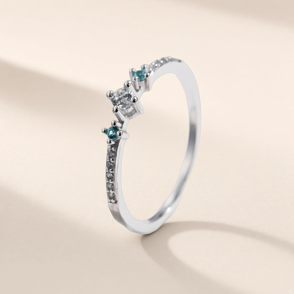 Bague Menthe à l'Eau argent 925, modèle trois pierres : zirconium cubique incolore entre deux pierres bleu-vert, sur fond crème