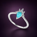 Bague Fontaine argent 925, goutte bleu-vert en pierre d'imitation sous une couronne de pierres claires, sur fond aubergine