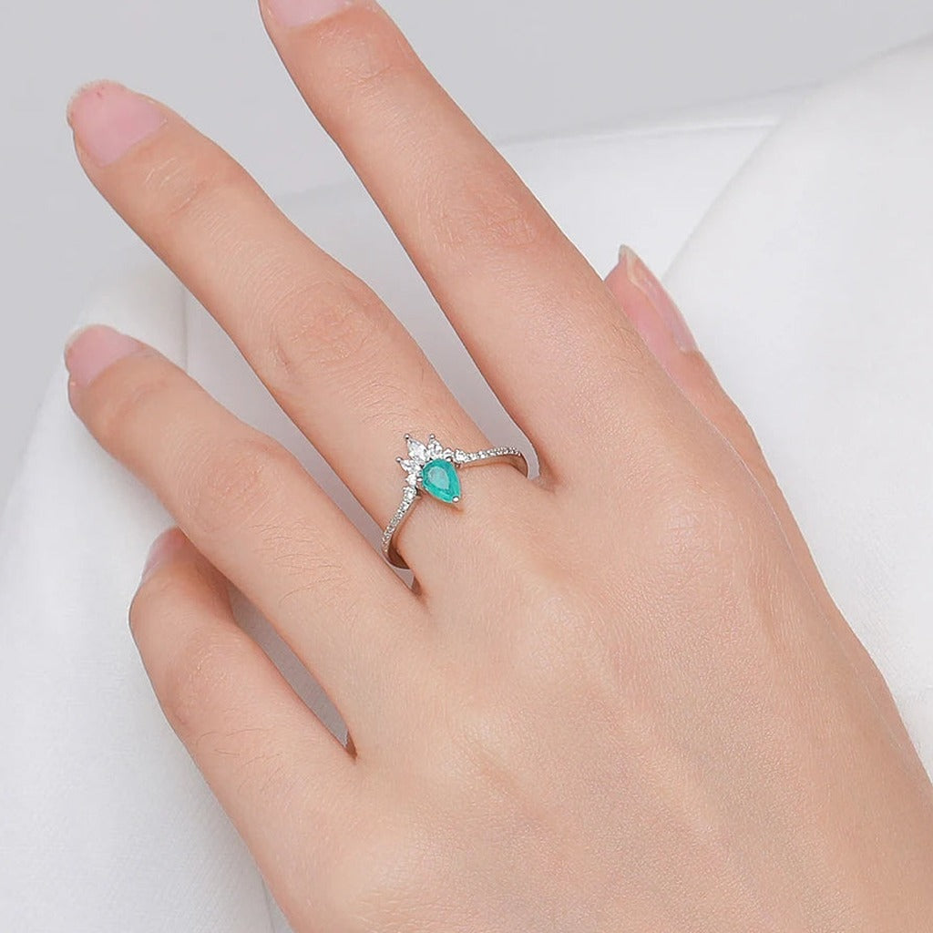 Bague Fontaine portée au doigt : la goutte bleu-vert sous sa couronne de pierres claires