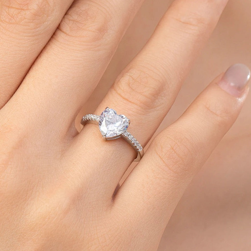 Bague Magnolia portée au doigt : le grand cœur incolore tenu par des griffes