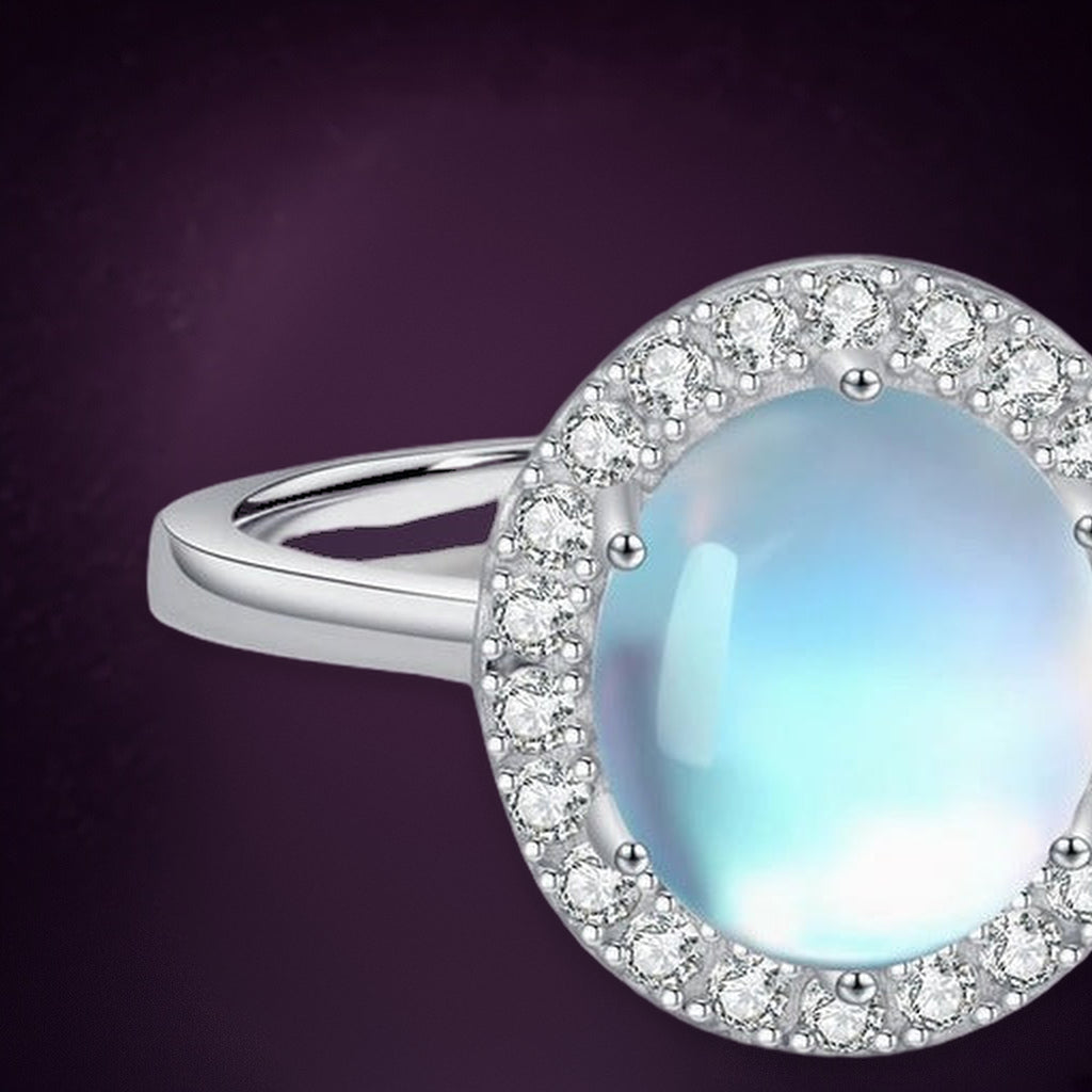 Bague Halo Lunaire en gros plan : cabochon ovale laiteux aux reflets bleus dans un halo de petites pierres claires