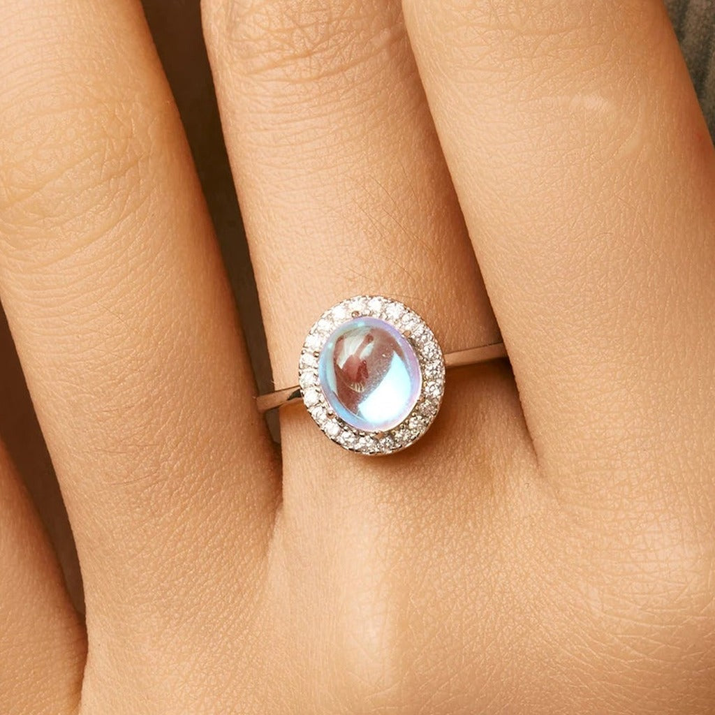 Bague Halo Lunaire portée au doigt : le cabochon ovale aux reflets bleus et son halo