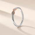 Bague Entrelacs argent 925, signe infini à finition dorée rose entre deux rangées de petits zirconiums cubiques clairs, sur fond crème