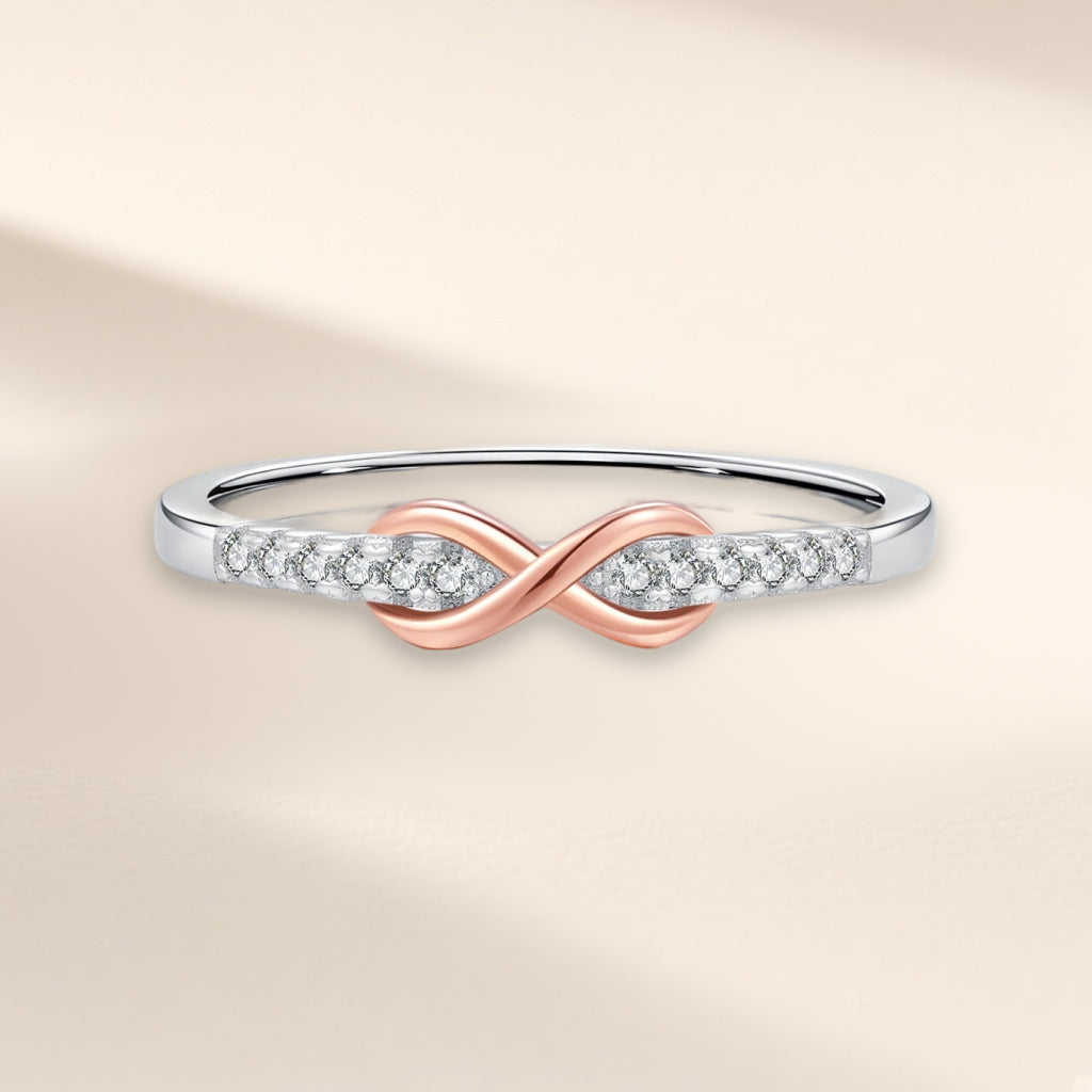 Bague Entrelacs vue de face : signe infini doré rose entre deux rangées de petites pierres claires