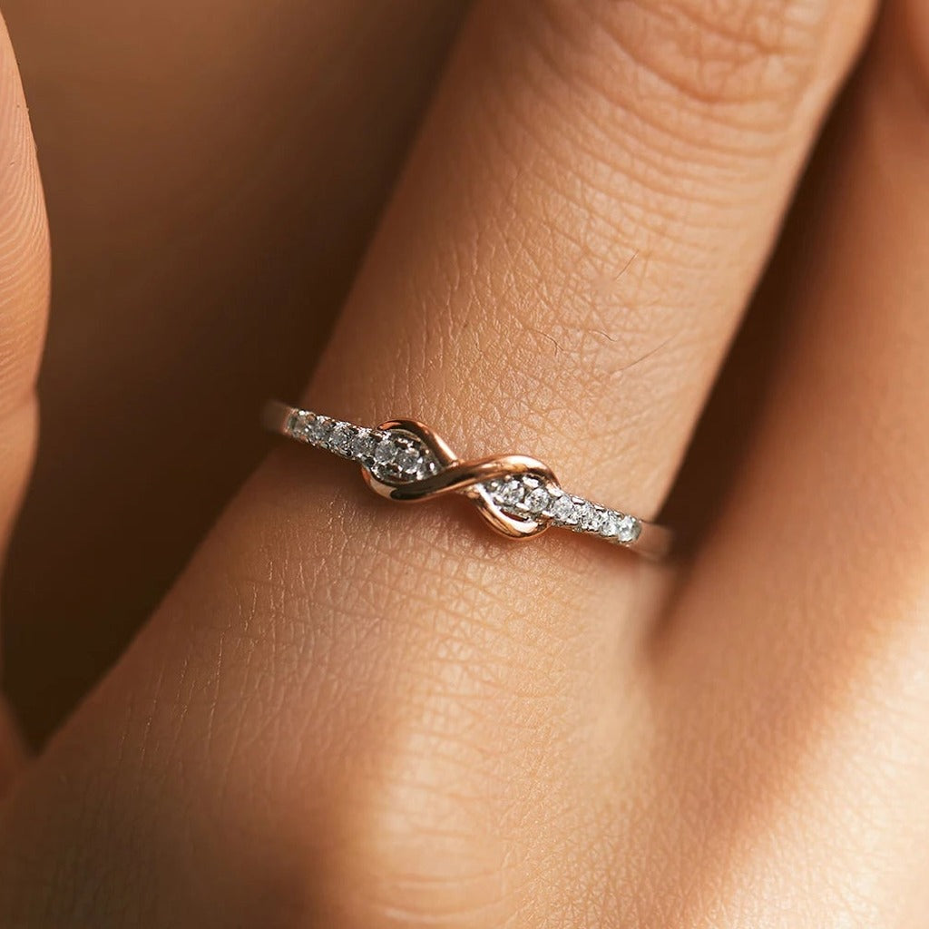 Bague Entrelacs portée au doigt : le signe infini doré rose au centre de l'anneau