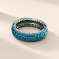 Bague Céleste argent 925, anneau large couvert de trois rangs de petites pierres d'imitation bleu turquoise tenues par des griffes, sur fond crème