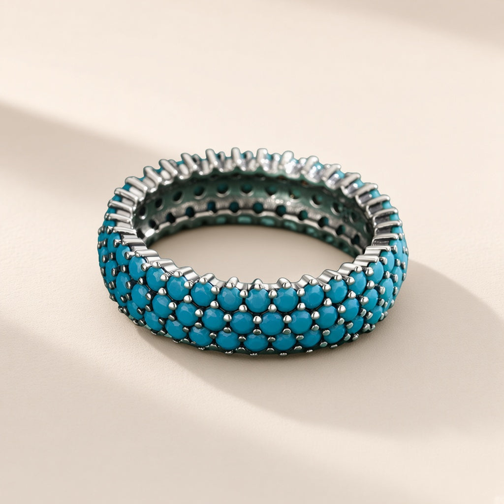 Bague Céleste argent 925, anneau large couvert de trois rangs de petites pierres d'imitation bleu turquoise tenues par des griffes, sur fond crème