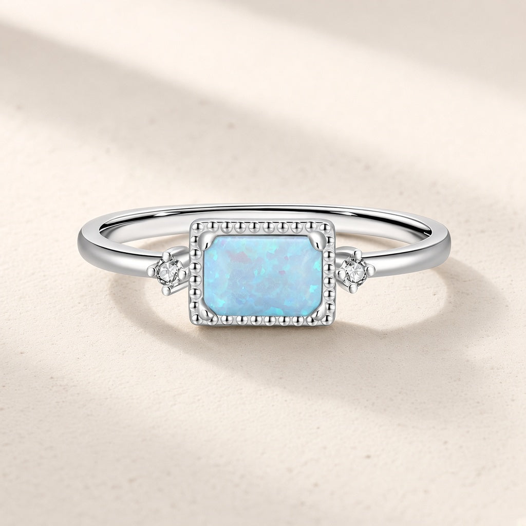 Bague Estampe argentée : pierre rectangulaire bleu pâle irisée dans un cadre perlé, une petite pierre claire de chaque côté
