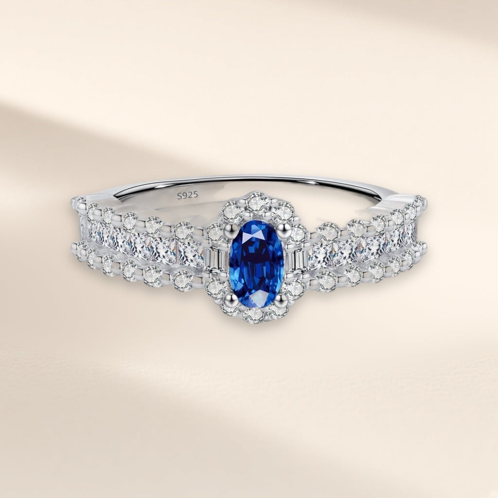 Bague Minuit vue de face : pierre ovale bleu roi entourée de petites pierres claires, anneau large serti