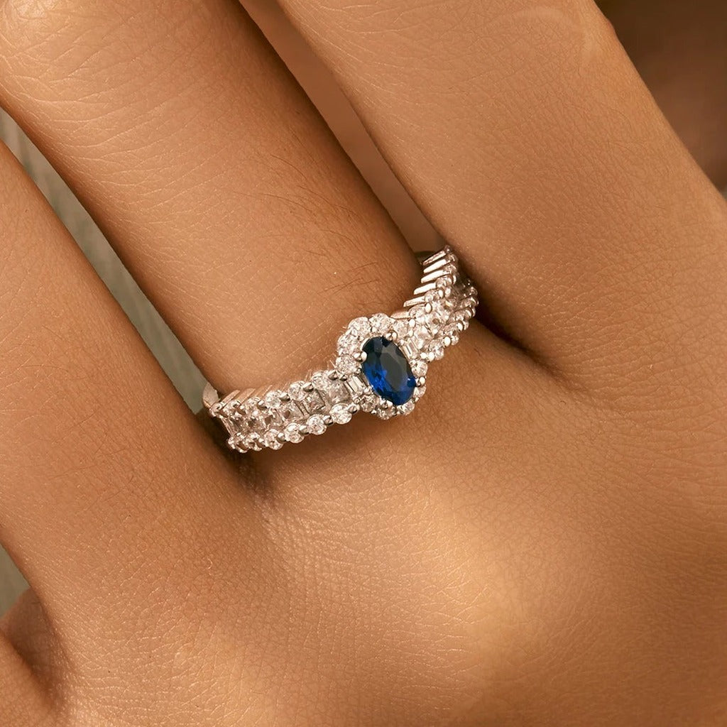 Bague Minuit portée au doigt : la pierre ovale bleu roi au centre de l'anneau serti