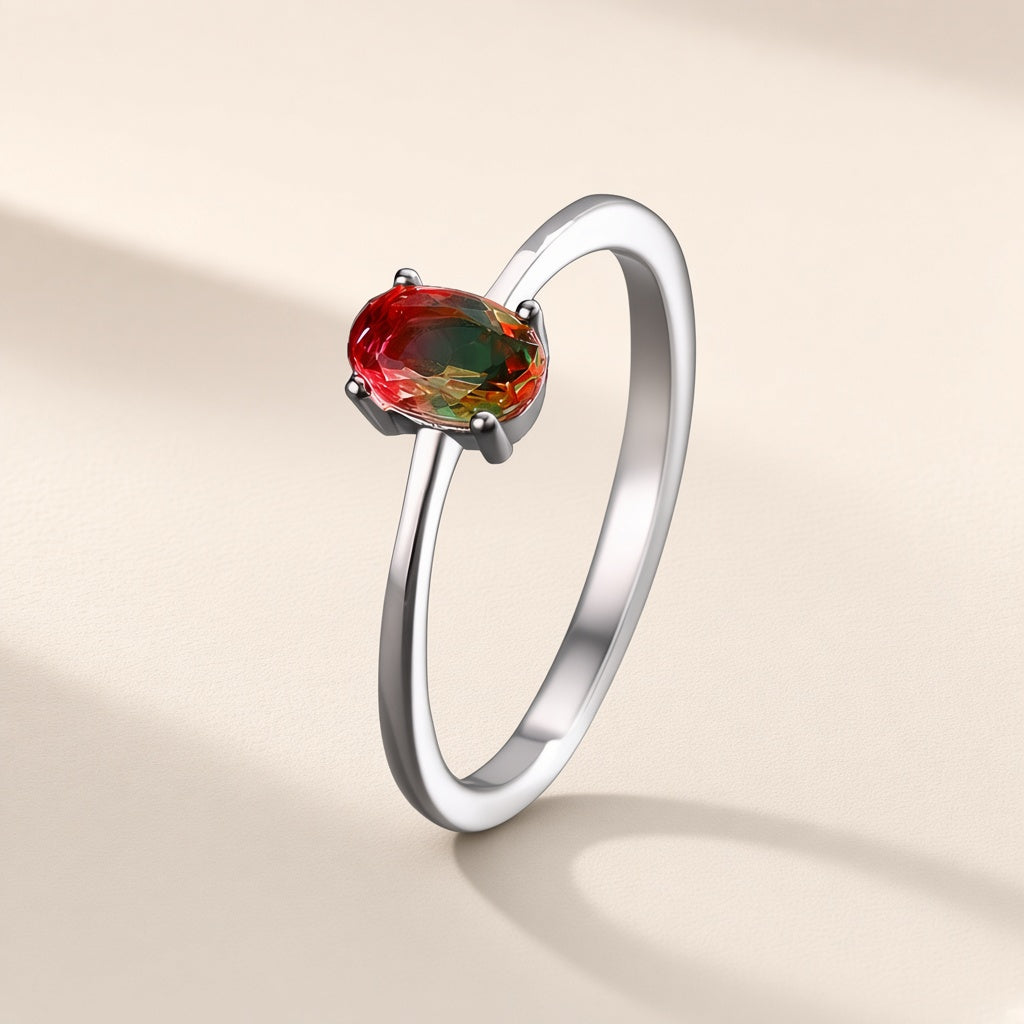 Bague Arrière-Saison argent 925, pierre d'imitation ovale rouge et verte tenue par quatre griffes sur un anneau fin, sur fond crème