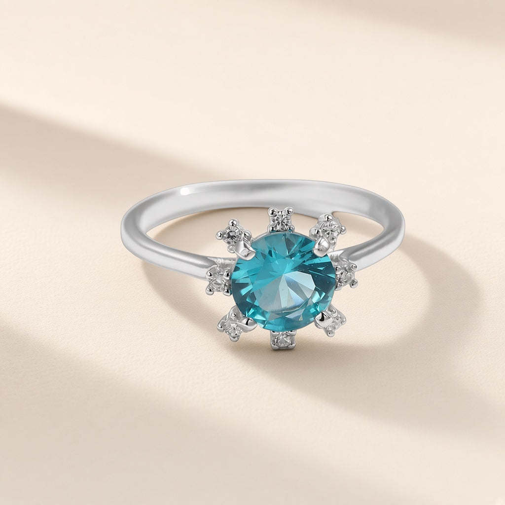 Bague Atoll argent 925, pierre ronde d'imitation bleu-vert entourée de petits zirconiums cubiques, sur fond crème