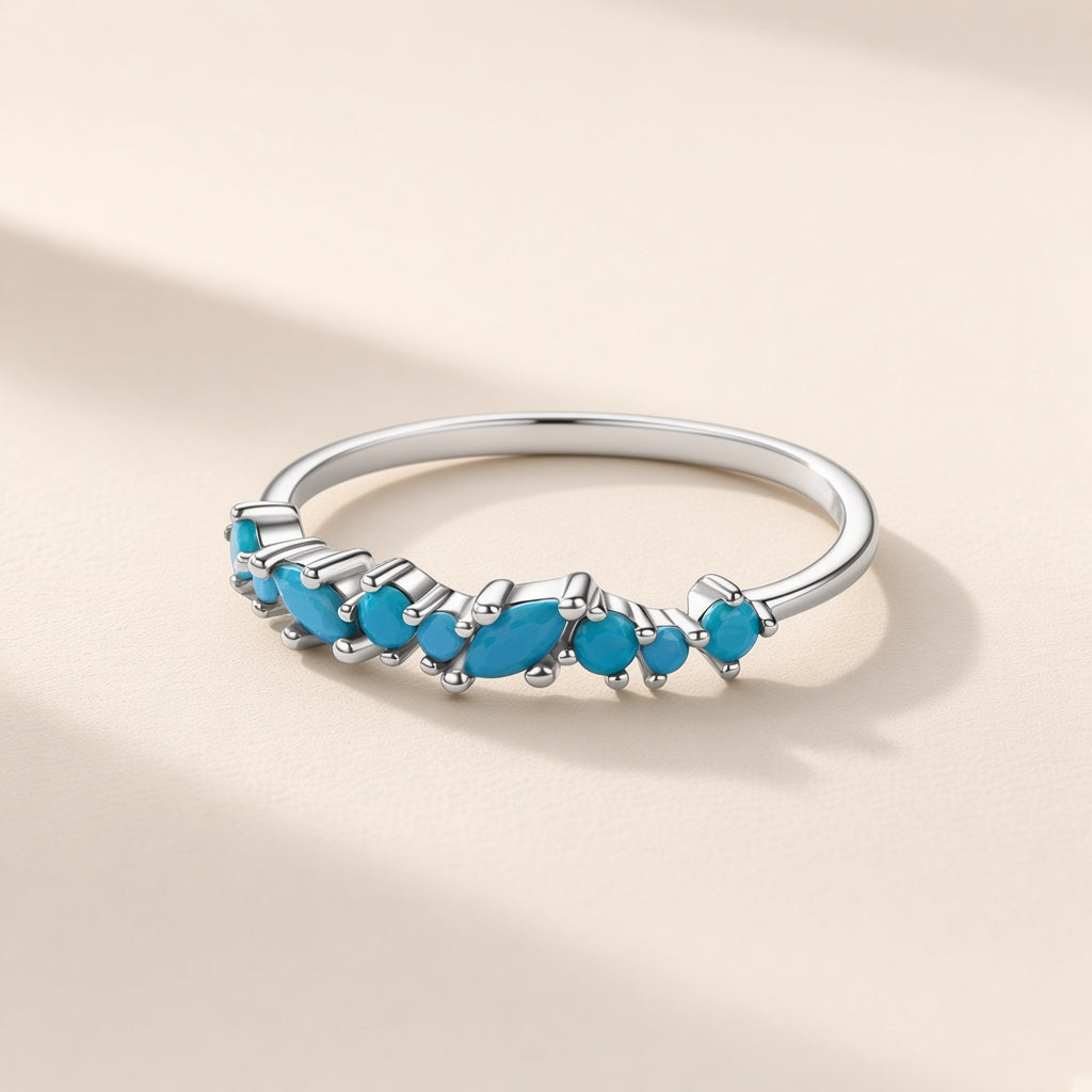 Bague Ressac argent 925, ligne de petites pierres d'imitation bleues en navette et rondes qui ondule sur l'anneau fin, sur fond crème