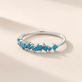 Bague Ressac argent 925, ligne de petites pierres d'imitation bleues en navette et rondes qui ondule sur l'anneau fin, sur fond crème