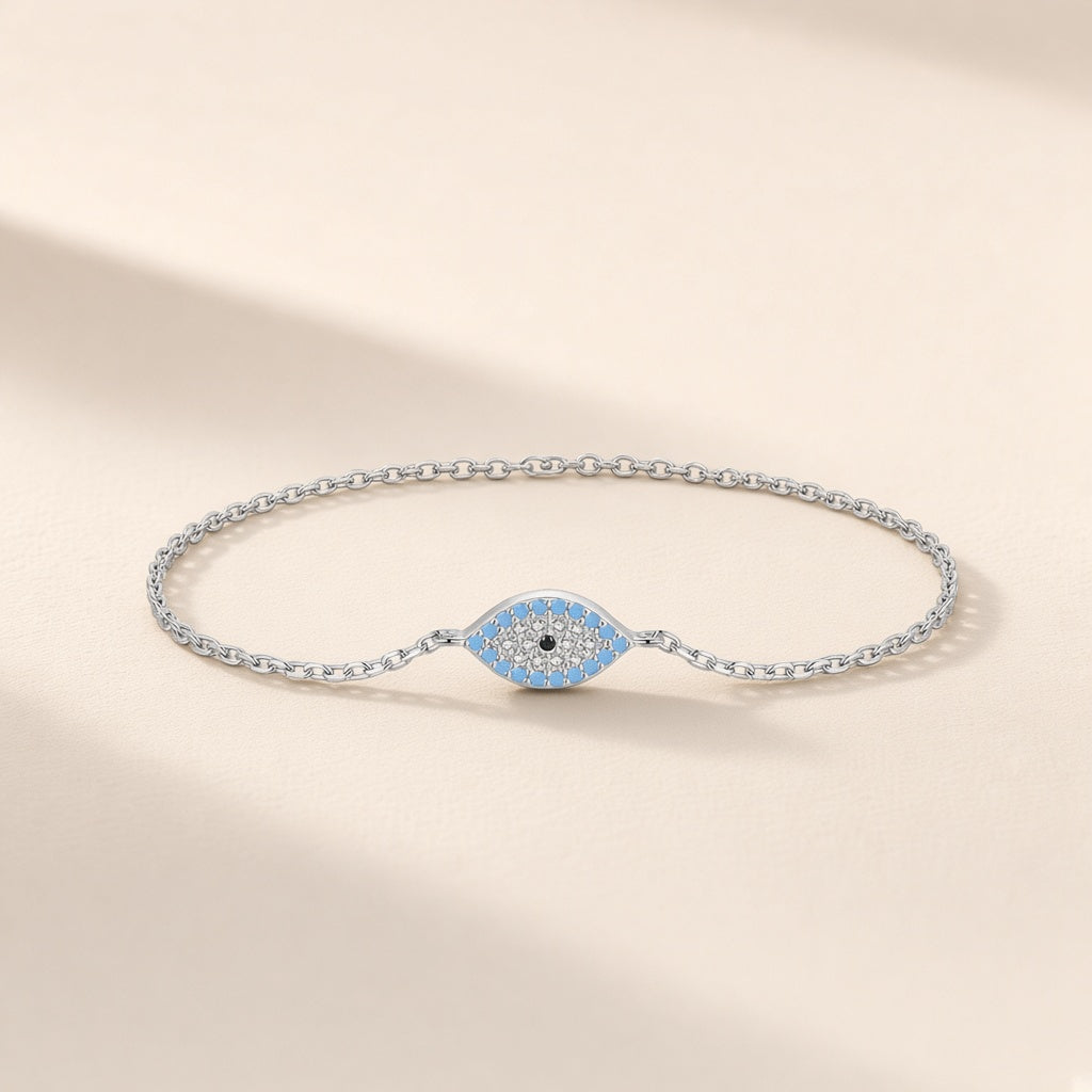Bracelet Regard d'Été argent 925, chaîne fine et œil en amande pavé de pierres d'imitation bleu turquoise et claires, pupille noire, sur fond crème