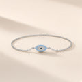 Bracelet Regard d'Été argent 925, chaîne fine et œil en amande pavé de pierres d'imitation bleu turquoise et claires, pupille noire, sur fond crème