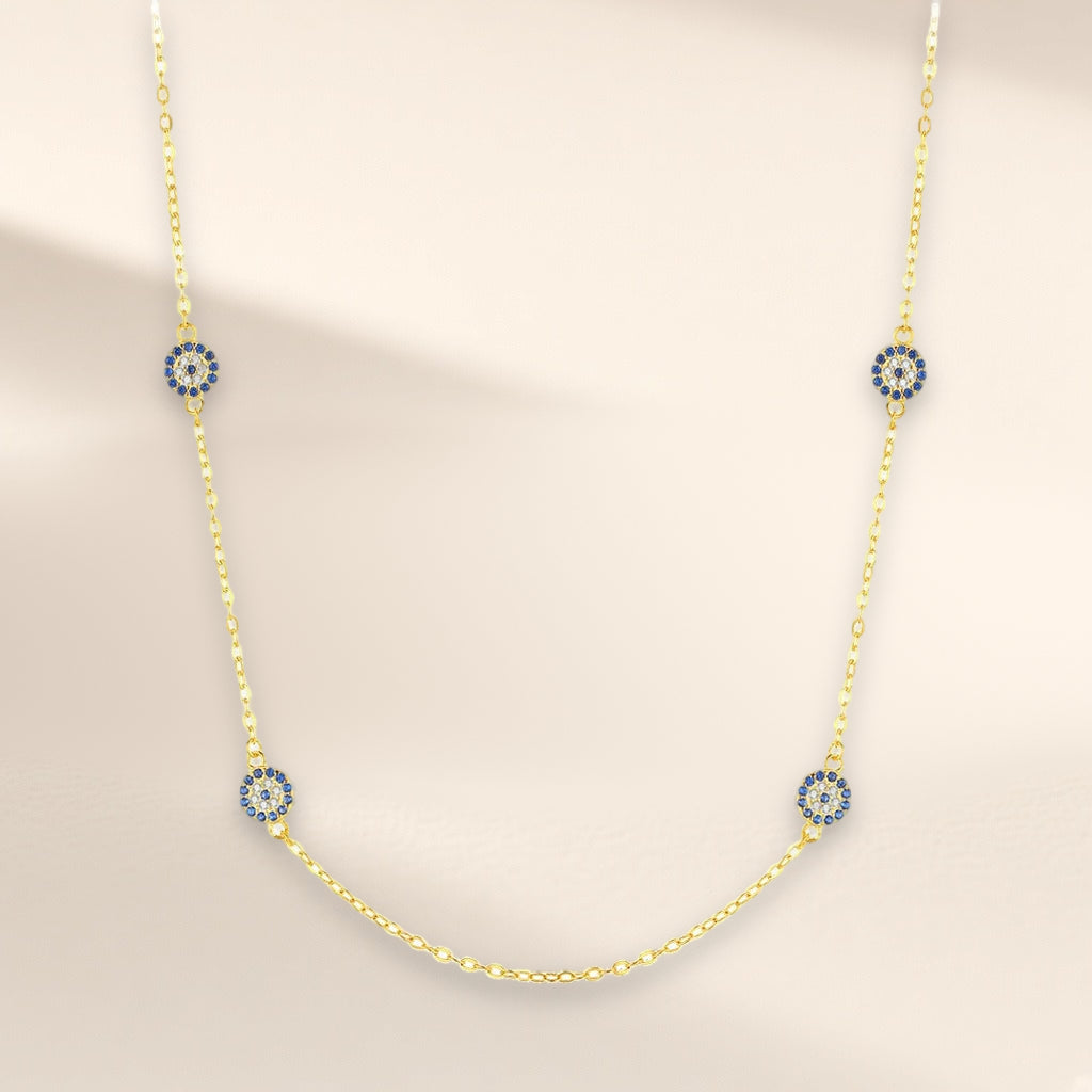 Collier Signe Bleu, finition dorée sur argent 925, modèle quatre médaillons : quatre petits médaillons ronds de pierres d'imitation bleues et claires, espacés sur la chaîne, sur fond crème