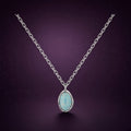 Collier Lune d'Écume argent 925, pendentif ovale en opale d'imitation bleutée dans un contour en vague, sur fond aubergine