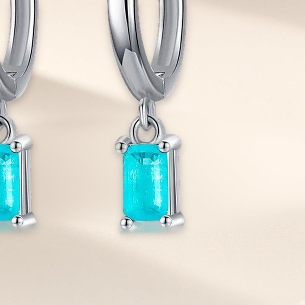Créoles Bleu Lagon en gros plan : la pierre rectangulaire bleu-vert tenue par quatre griffes sous l'anneau
