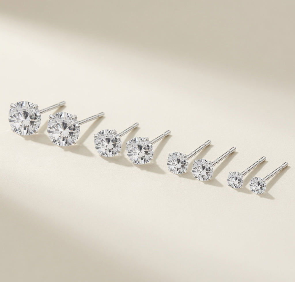 Puces Point du Jour Luminori en argent 925, solitaire zirconium décliné en quatre tailles de 4 à 7 mm, gamme posée sur fond crème lumineux