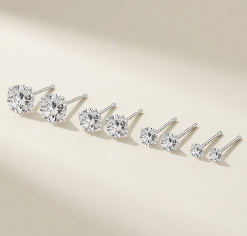 Puces Point du Jour en argent 925, solitaire en zirconium cubique décliné en quatre tailles de 4 à 7 mm, gamme posée sur fond crème lumineux