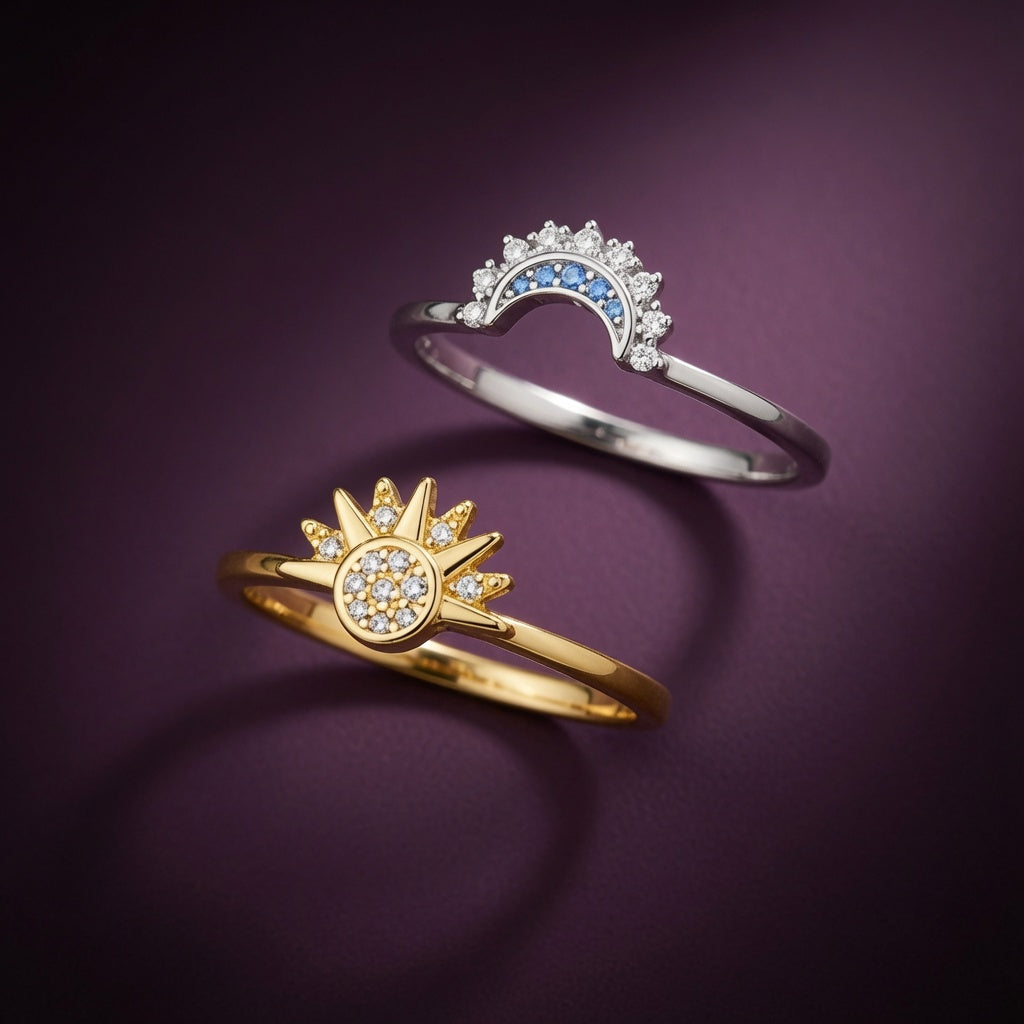 Duo de bagues Soleil et Lune Luminori posées côte à côte sur fond aubergine : soleil rayonnant doré et croissant de lune argenté, serti de zircon