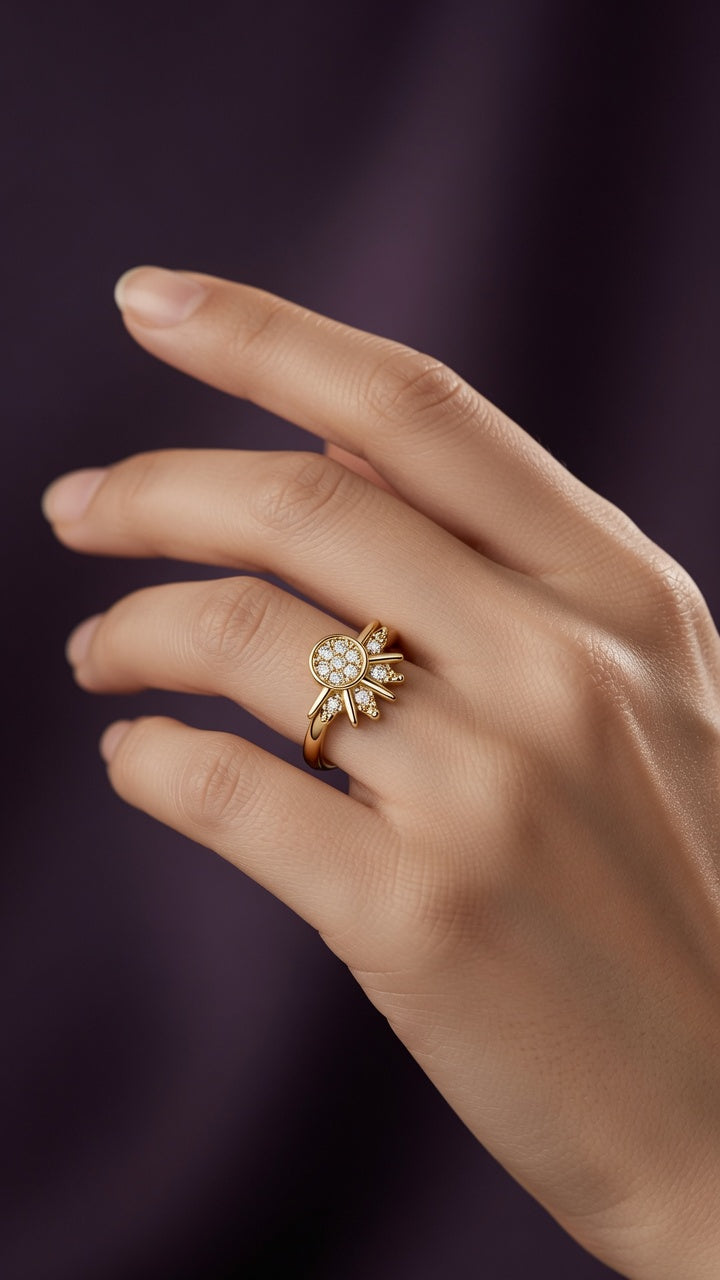 Bague Soleil dorée portée à l'annulaire, rayons fins et pavé de zircon au centre, porté épuré sur fond aubergine