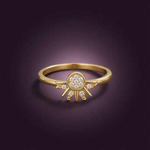 Bague Soleil Luminori en gros plan, disque solaire doré aux rayons pointus et centre pavé de zircon, sur fond prune profond
